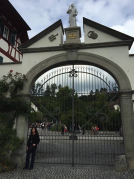 Tanya at the front gate with Saint Bruno.   The rectangular item flanking his statue is called a "roost" (our last name)… aka a special rack used to roast martyrs. <hr> Tanya vor dem schmideisernen Eingangstor.